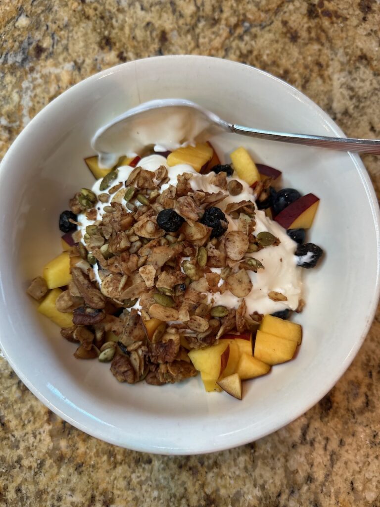 Granola, a cut up peach, blueberries and plain yogurt 