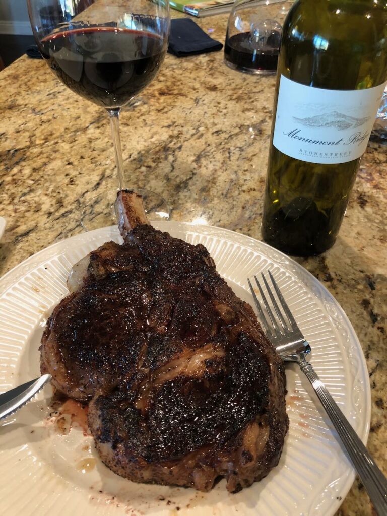 Cowboy steak cooked and on a plate ready for dinner with a nice glass of cabernet