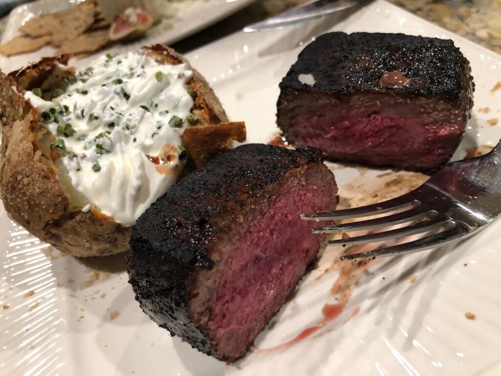 Perfectly cooked rare steak with a thin crust on the outside served with a baked potato