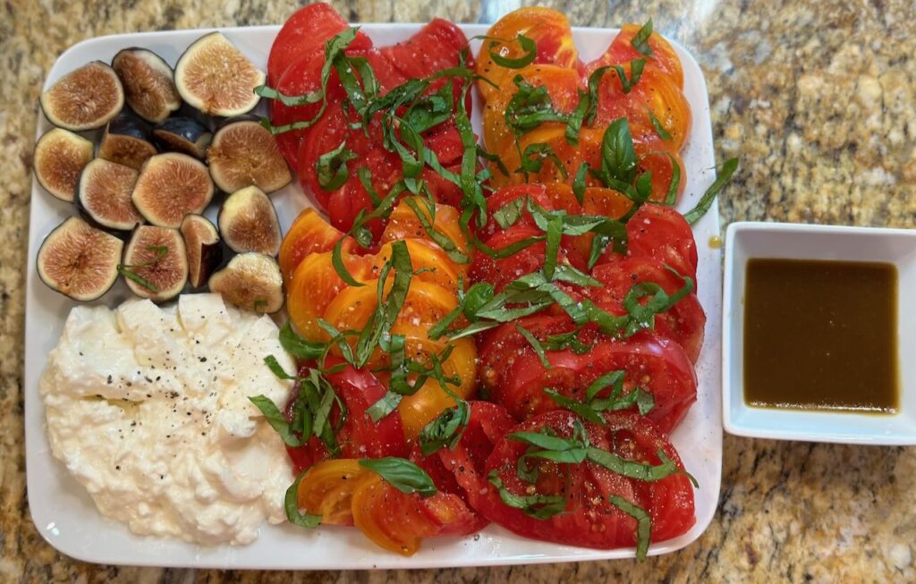 Prepared appetizer of sliced figs, S&P burrata, sliced heirloom tomatoes with basil chiffonade and balsamic viniagrette