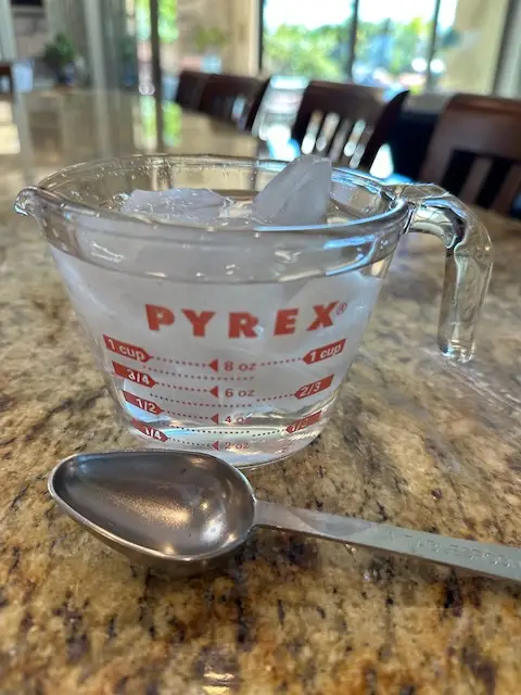 Pyrex measuring cup with ice water in it - and a tablespoon beside it.